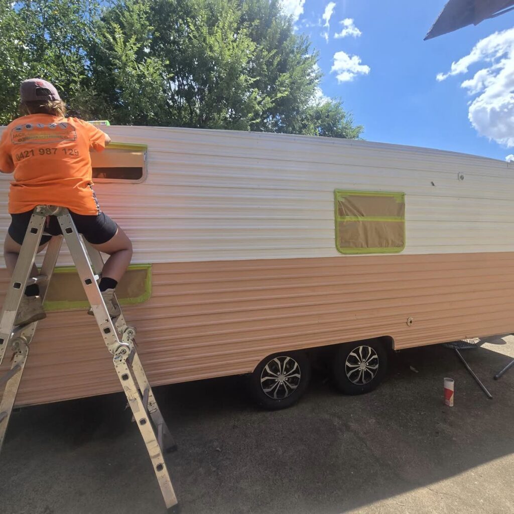 Worker on a ladder masking a caravan exterior ready for painting