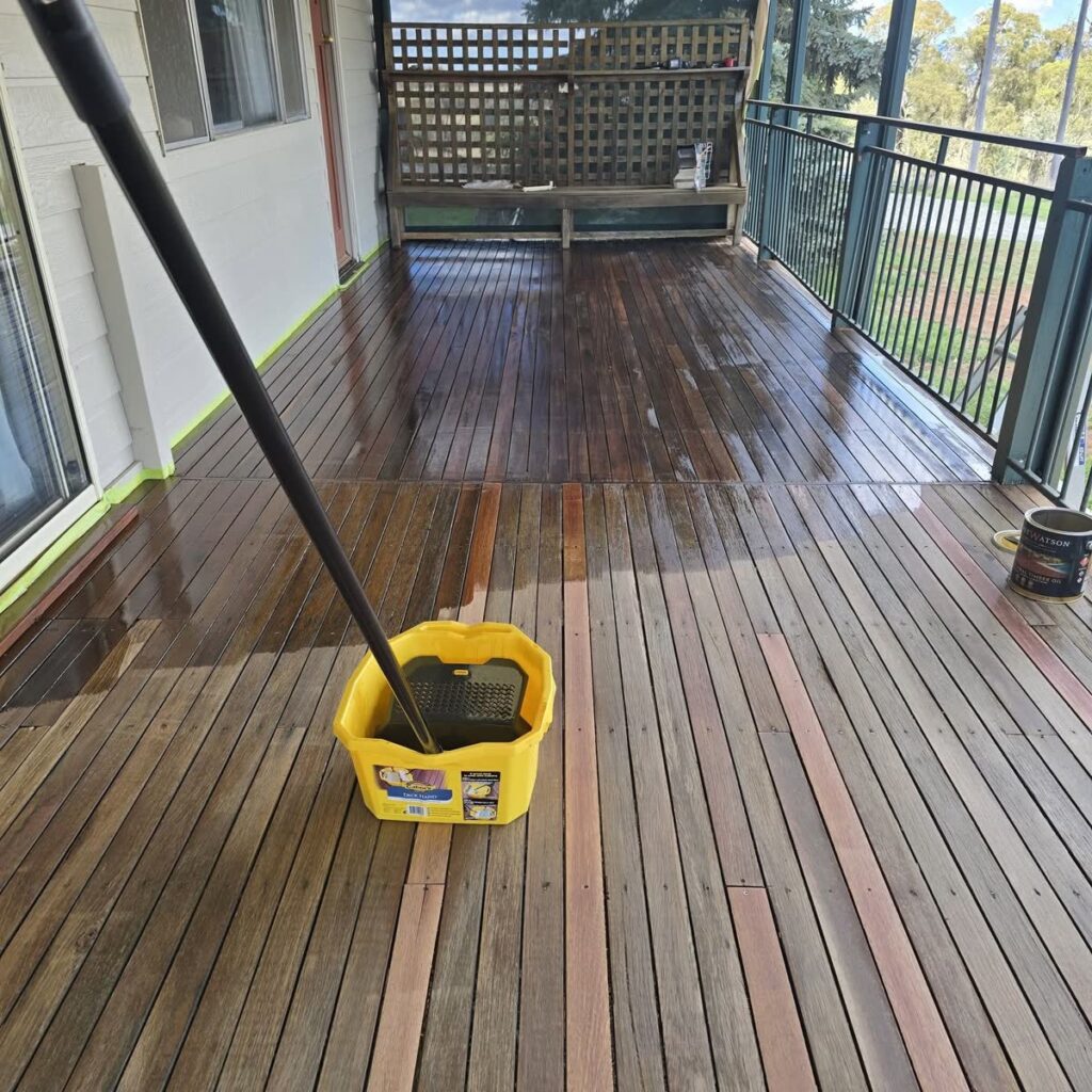 Applicator pad and tin of decking oil on a half-oiled timber verandah