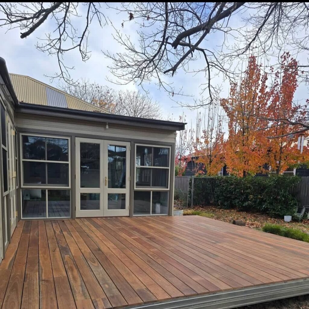 Oiled timber deck outside a sunroom with autumn trees behind