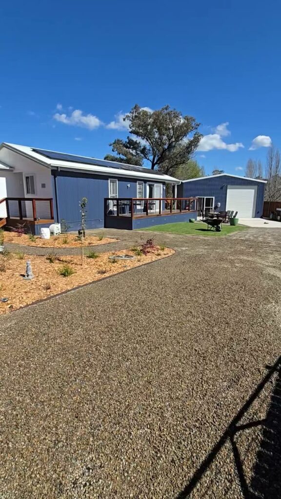 Front yard of a blue weatherboard home with new garden beds, mulch, gravel and a strip of turf