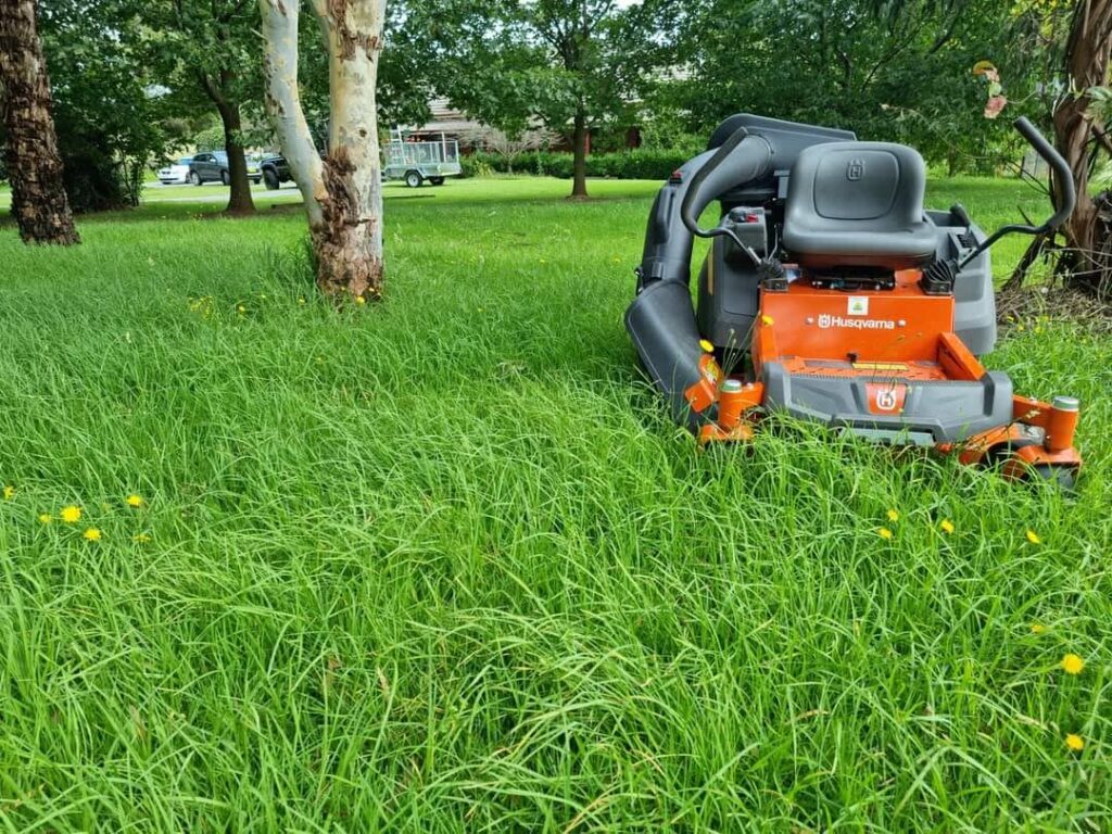 Orange Husqvarna zero-turn mower on a freshly cut lawn under trees