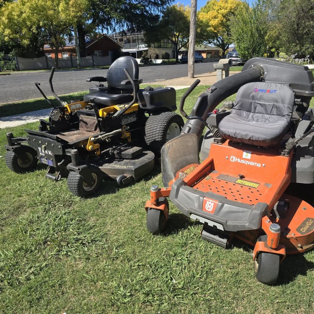 Two zero-turn ride-on mowers parked on a nature strip in Orange
