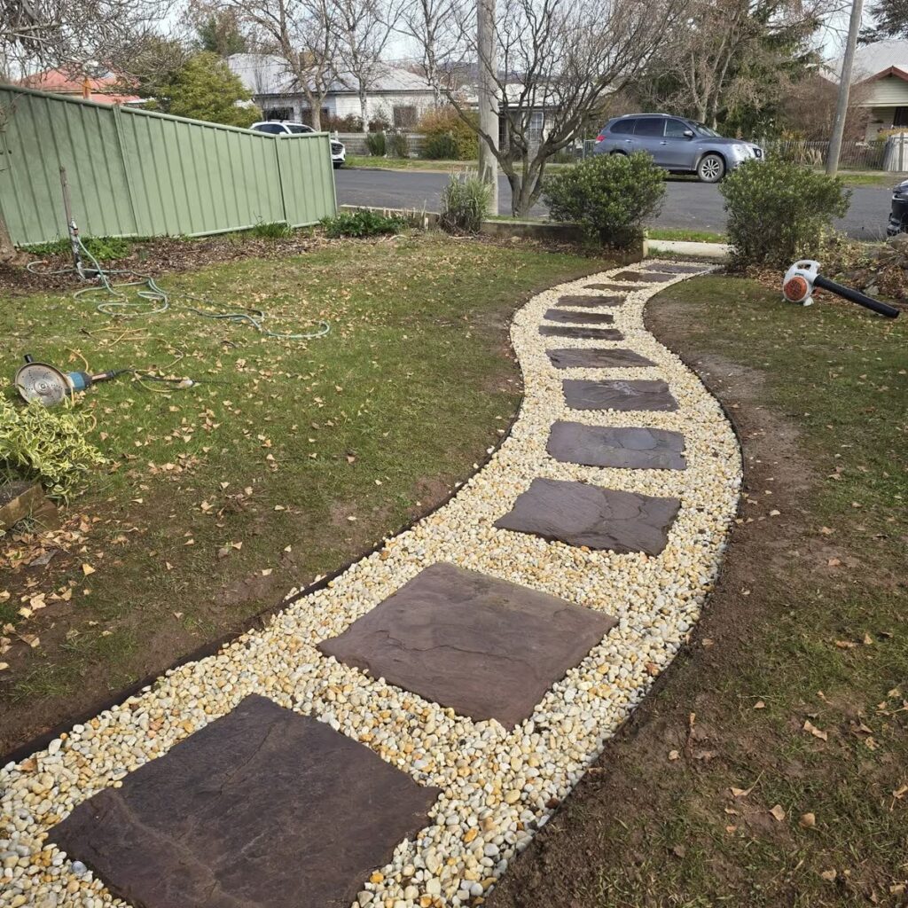 Stepping stones set into decorative pebbles between garden beds beside a lawn
